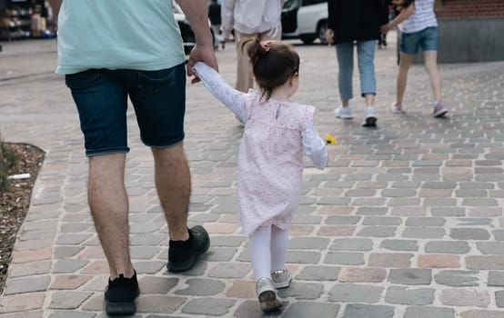 A young caucasian father is holding his little daughter and walking along the city street on a spring afternoon,close-up side view.Concept of walking people from the back.