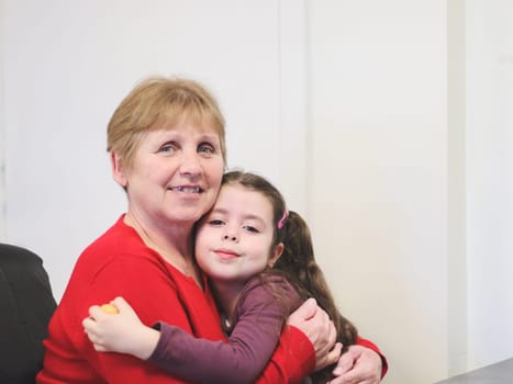 Portrait of a beautiful Caucasian brunette girl in the arms of a happy woman grandmother sitting at a table indoors, close-up side view with depth of field.