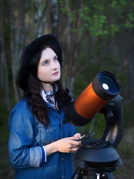 Portrait of young woman looking through the telescope on the hil