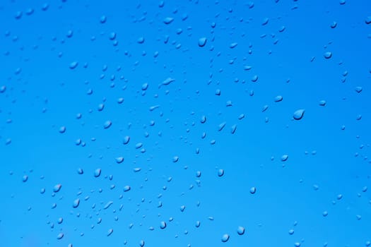 Raindrops on the surface of window glass with a blurred background.