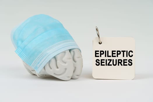 Medical concept. On a white surface next to the brain there is a notepad with the inscription - epileptic seizures