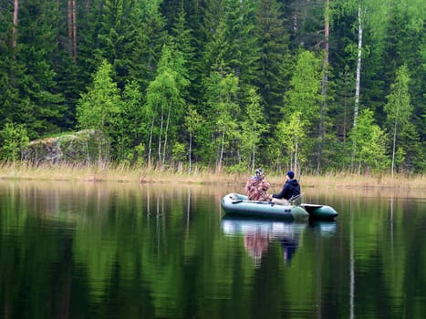 Two men catch fish from an inflatable boat with fishing rods on the lake in the summer
