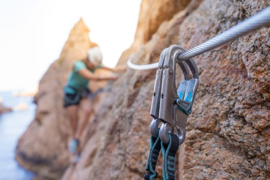 Pretty female climber strong success hiking on rocks over the sea with rope and helmet. High quality photo