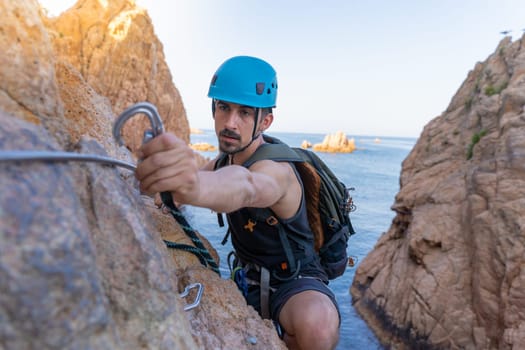 Young male climber strong success hiking on rocks over the sea with rope and helmet. High quality photo