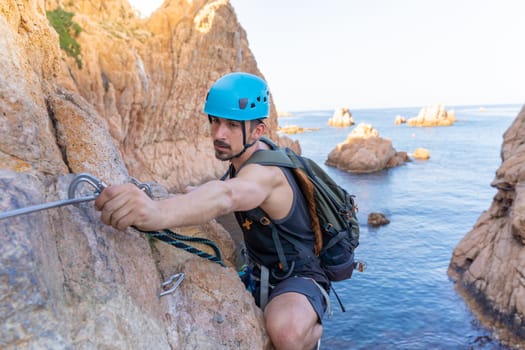 Young male climber strong success hiking on rocks over the sea with rope and helmet. High quality photo