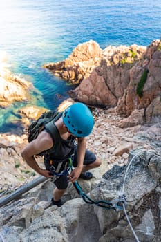 Young male climber strong success hiking on rocks over the sea with rope and helmet. High quality photo