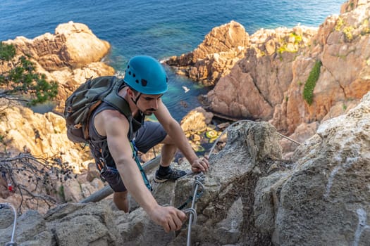 Young male climber strong success hiking on rocks over the sea with rope and helmet. High quality photo