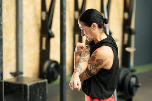 Side view of a mature strong woman with tattoos warming up in a cross training center