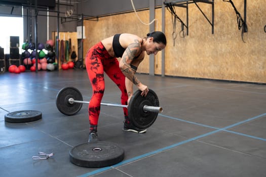 Woman adding weights in a bar to dead-lift in a cross training gym