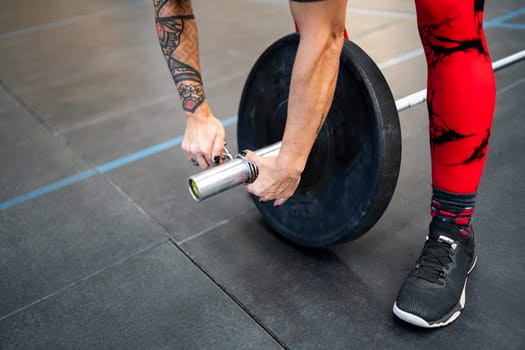 Top close-up view of a woman securing a clamp at the end of a weightlifting bar