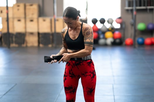 Mature modern woman with tattoos putting on a belt to prevent injuries while lifting deadlifts