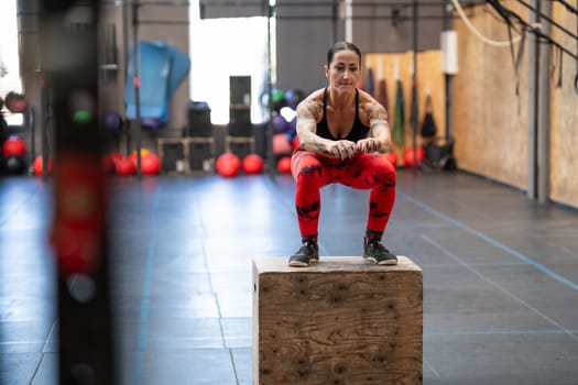 Strong tattooed woman jumping on a box in a cross training center