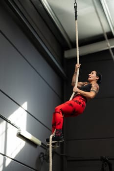 Vertical photo of a strong woman climbing rope in a cross training gym