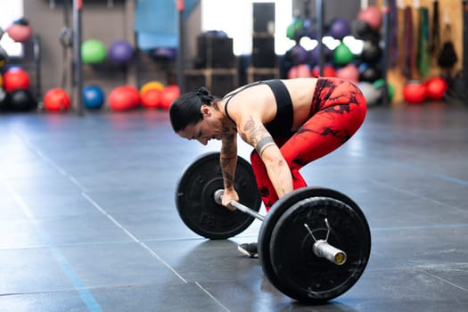 Horizontal photo of a sportive woman about to lift weight with bar in a gym