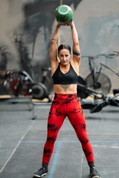 Vertical frontal portrait of a woman lifting a kettlebell standing in a cross training gym