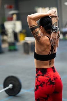 Rear view of a strong female athlete stretching after working out in a gym