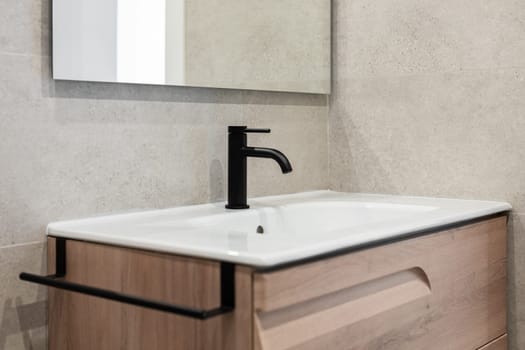 Close-up of a sink with a black tap and a mirror on the background of a gray stone wall. Concept new and stylish plumbing in new residential complexes ready for delivery.
