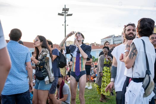 Lisbon, Portugal. 17 June 2023: Homosexual man blowing soap bubbles at Pride Parade. Young slim gay with rainbow painted torso having fun at lgbtqia pride event. Sexual equality, diversity, pride LGBTQ