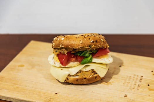 Fresh breakfast bagel bun with seeds with hummus and cheese eggs tomato and salad lying on wooden board