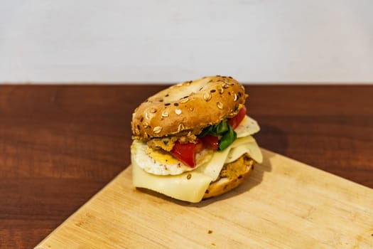 Fresh breakfast bagel bun with seeds with hummus and cheese eggs tomato and salad lying on wooden board