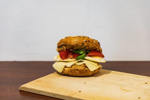 Fresh breakfast bagel bun with seeds with hummus and cheese eggs tomato and salad lying on wooden board