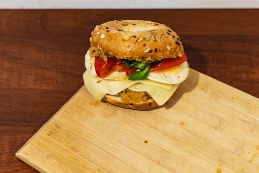 Fresh breakfast bagel bun with seeds with hummus and cheese eggs tomato and salad lying on wooden board