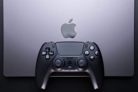 BERLIN , GERMANY - JANUARY 14 2024: Dualsense PS5 game controller placed near an Apple MacBook Pro Space Black for gaming.
