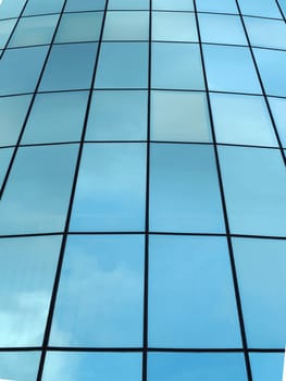 modern glass facade of a skyscraper in perspective with reflected clouds.