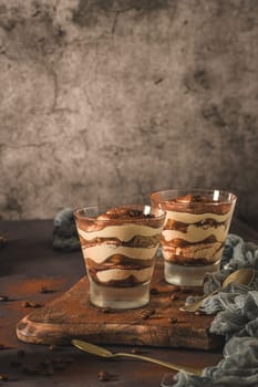 Delicious italian dessert tiramisu in a glasses on a dark slate, stone or concrete background.