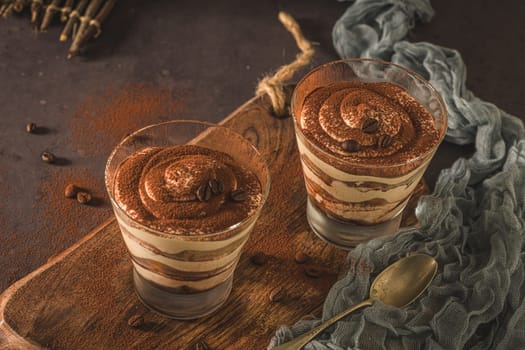 Delicious italian dessert tiramisu in a glasses on a dark slate, stone or concrete background.