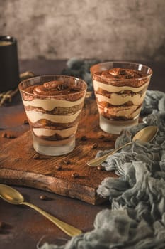 Delicious italian dessert tiramisu in a glasses on a dark slate, stone or concrete background.