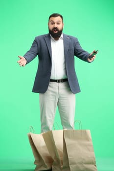 A man, full-length, on a green background, with a phone.