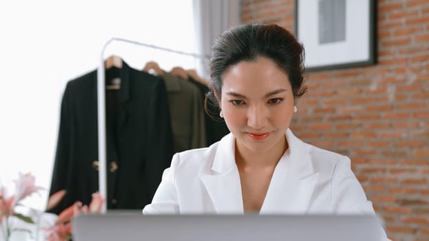 Young businesswoman sitting on the workspace desk using laptop computer for internet online content writing or remote working from home. Clothing and textile business marketing analysis. Vivancy