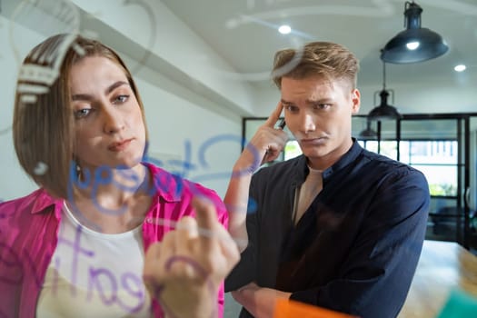 Couple of businesspeople discussing and brainstorming about solving marketing problem in front of glass board at business meeting by using mind map and sticky notes. Working together. Immaculate.