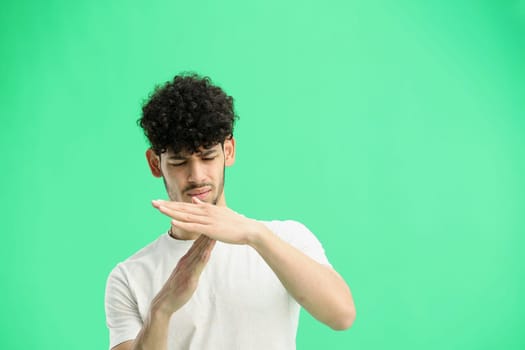 A man, on a green background, in close-up, shows a pause sign.