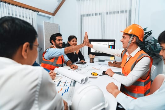 Diverse group of civil engineer and client celebrate and high five after make successful agreement on architectural project, reviewing construction plan and building blueprint at meeting table.Prudent