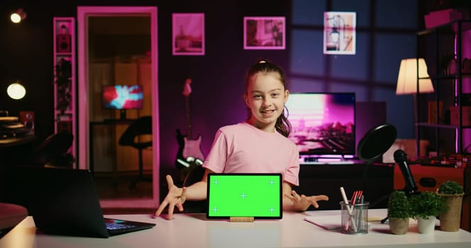 Smiling daughter filming online content with her parent using green screen tablet from sponsoring brand. Happy kid and her mother do internet videos for fans using chroma key device