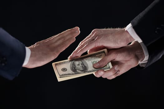 A man's hand in a black suit holds out a wad of money, which refuses. On a black background