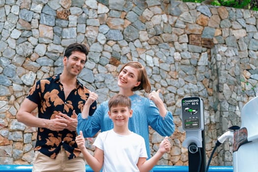 Family road trip vacation with electric vehicle, lovely family recharge EV car with green and clean energy. Stone seawall background and eco friendly car travel for sustainable environment. Perpetual