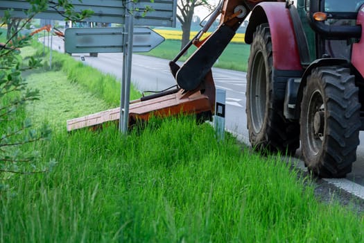 After grass cutting, roadside looks neat and well-maintained. Tractor equipped with cutting attachment is mowing field.