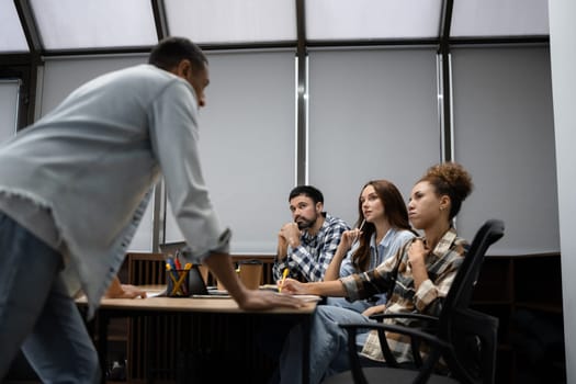 Group of diverse businesspeople using a laptop while working together in a modern workspace.