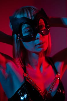 Blonde woman putting on leather mask in bedroom in red blue neon light