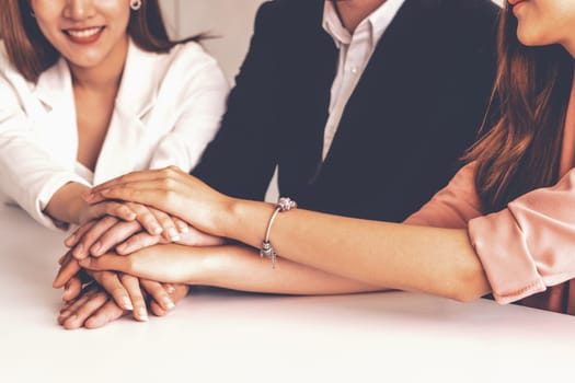 Businessmen and businesswomen joining hands in group meeting at multicultural office room showing teamwork, support and unity in business. Diversity workplace and corporate people working concept. uds