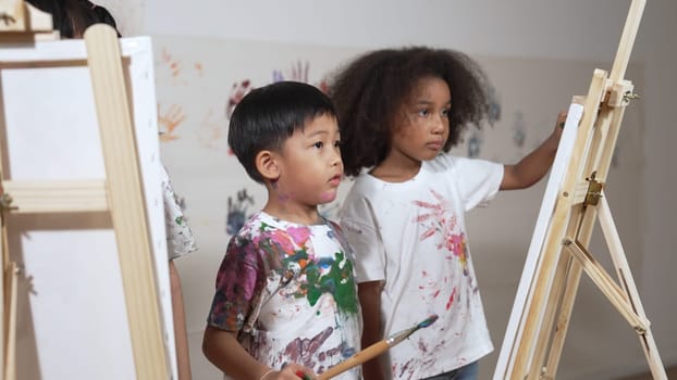 Happy creative african girl painted or draw canvas together with asian boy. Group of playful student create funny painting or artwork painted by watercolor. Creativity activity concept. Erudition.