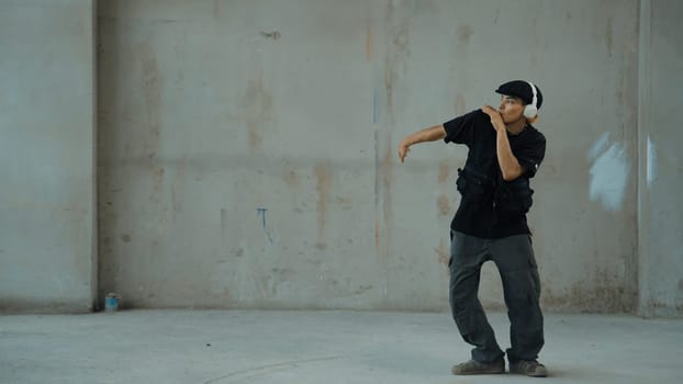 Handsome hipster practicing break dancing while listening music from headphone with cement background. Motion shot of street dancer perform robot dance. Outdoor sport 2024. Modern dance. Endeavor.