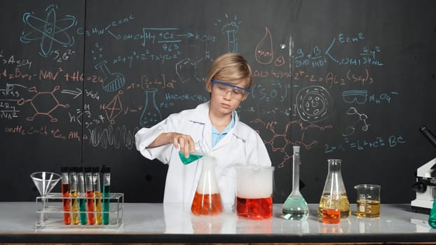 Smart boy inspect mixed chemical liquid in laboratory beakers while holding and looking carefully. Caucasian child focus on doing an experiment in chemistry lesson or STEM science class. Erudition.