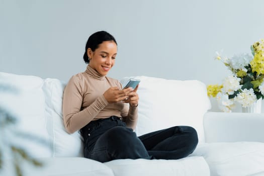 Relaxed young African American woman using crucial mobile phone on sofa couch in living room at home