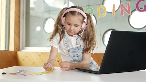 Pretty girl wearing headphone while study electronic equipment. Caucasian child doing science experiment while laptop, screwdriver and wires placed near on table. Smart online classroom. Erudition.