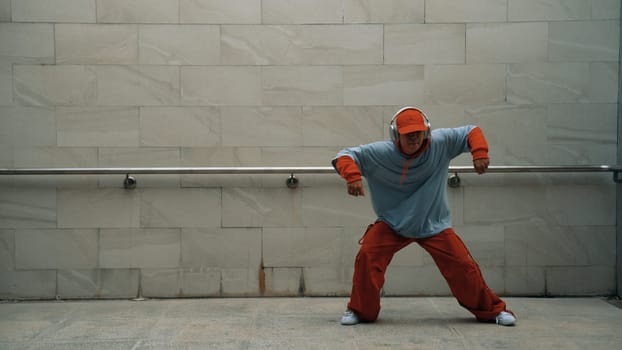 Handsome choreographer practice street dance in gray background. Young attractive b-boy dancer perform while wearing stylish cloth. Feeling of lively step. Copy space. Outdoor sport 2024. Sprightly.