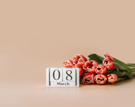 International women's day or eight march concept with copy space. 8 march date on perpetual calendar and bunch of red tulip on beige champagne background